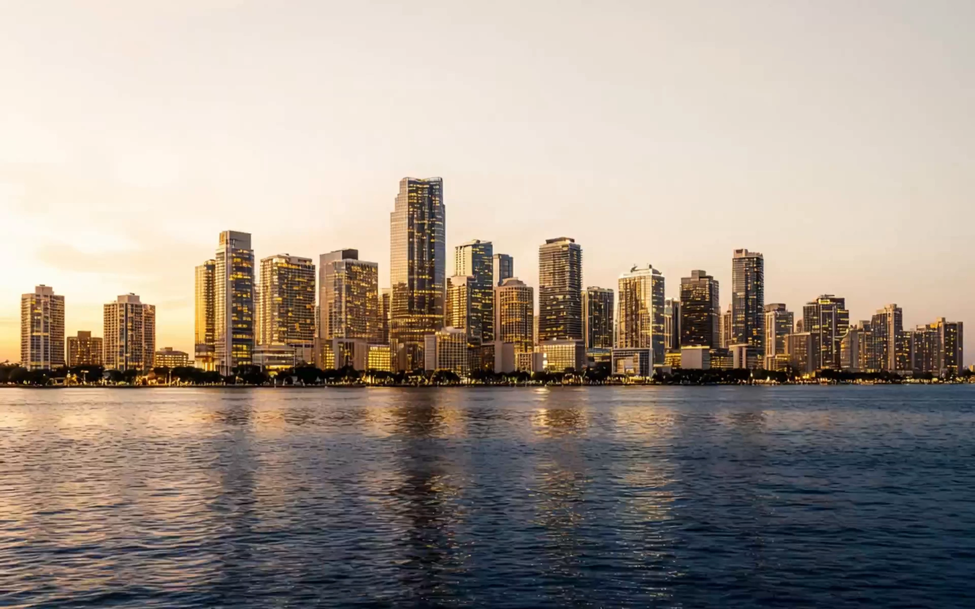 Editorial dusk render derived from developer materials of Miami's lit residential towers along the bay — ivory sky, golden light on the water, no people.